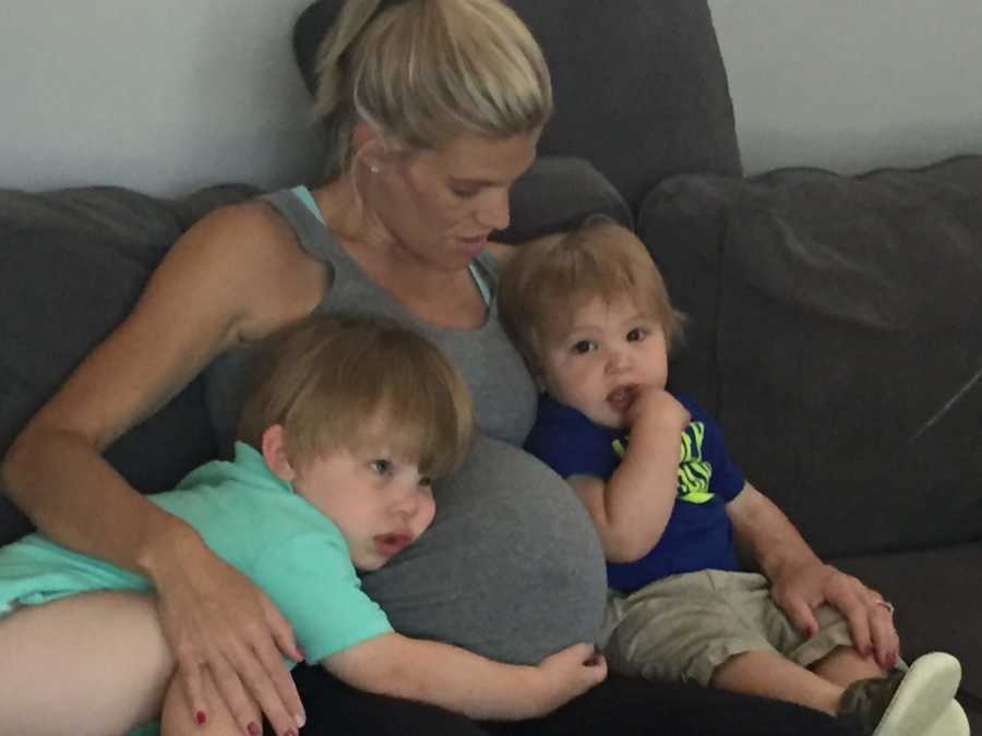 A pregnant mother sits on the couch with two of her sons
