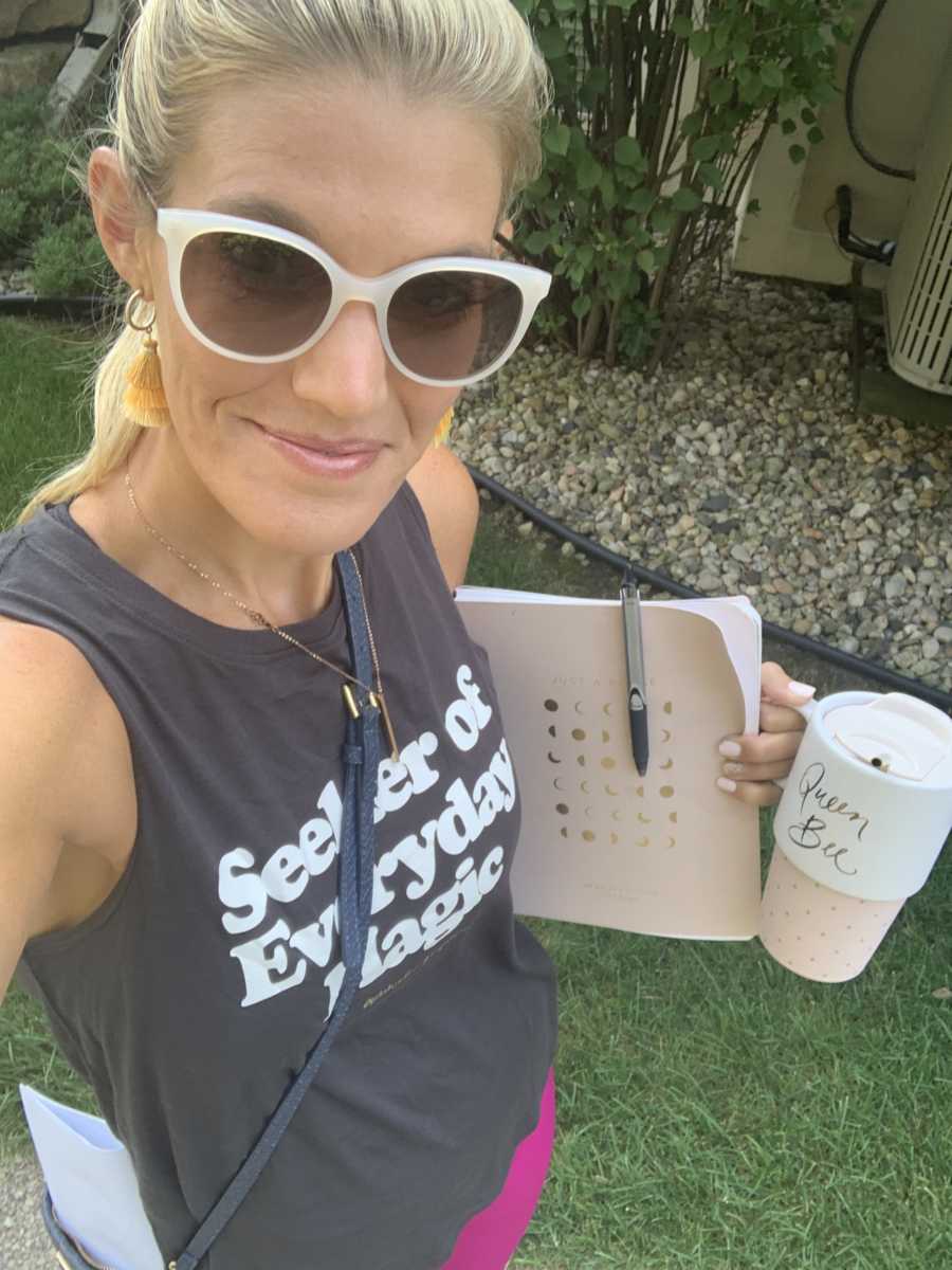 A woman stands holding a planner and a coffee cup