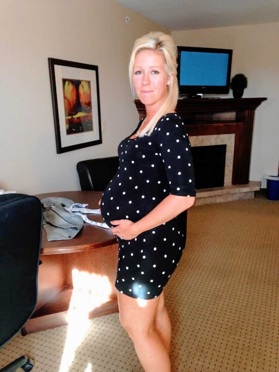 Young woman pregnant with her rainbow baby after a miscarriage smiles in a black and white polka dot dress