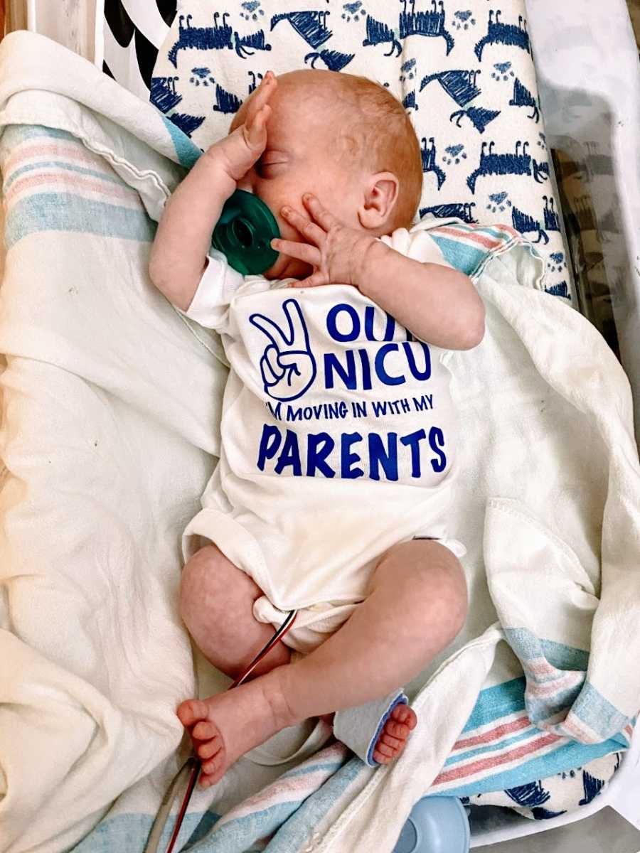 Mom takes photo of NICU baby wearing a one that says "Peace out NICU I'm moving in with my parents"