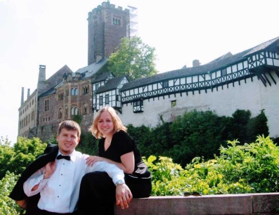 Young couple in fancy attire take a photo together in front of a beautiful, huge building