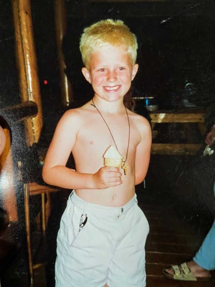 Little boy with blond hair smiles big for a photo while holding a cake cone with vanilla ice cream