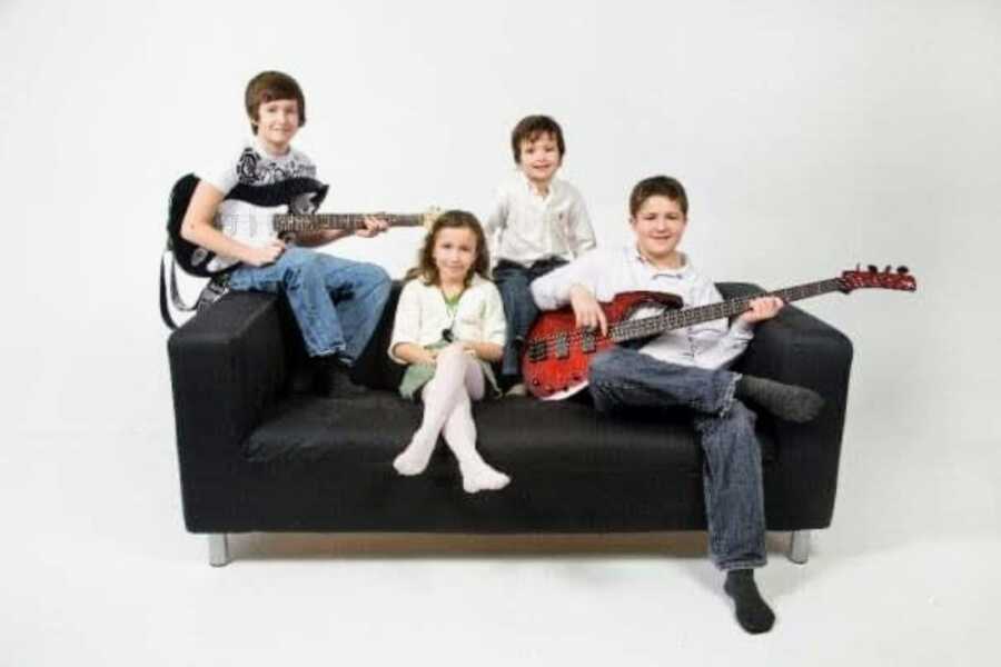 Mom of four takes photos of her three sons and one daughter sitting on a couch together, two sons holding electric guitars