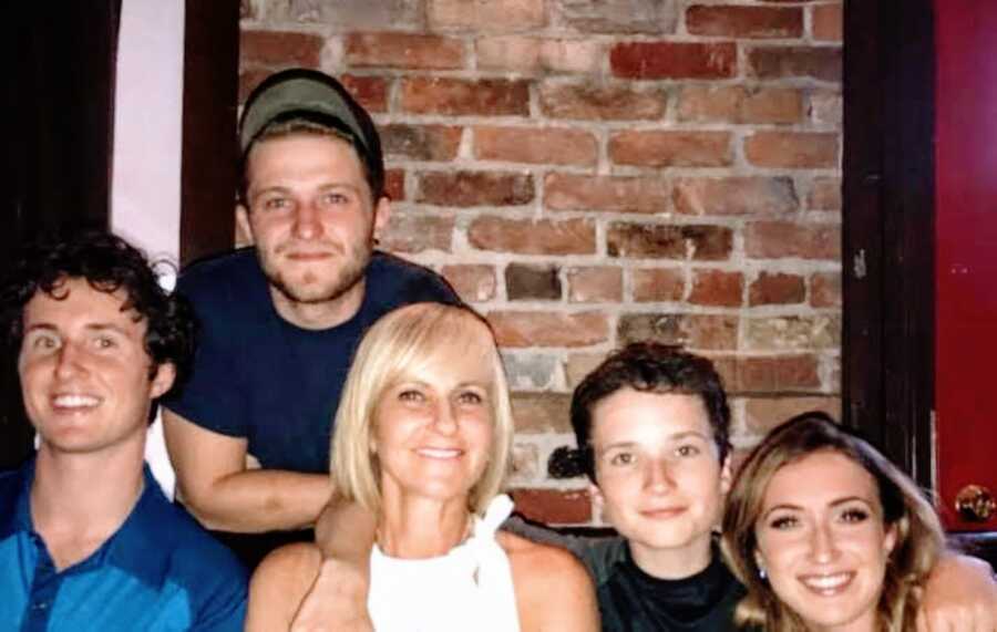 Mom of four smiles big for a photo with all of her children while out for dinner together