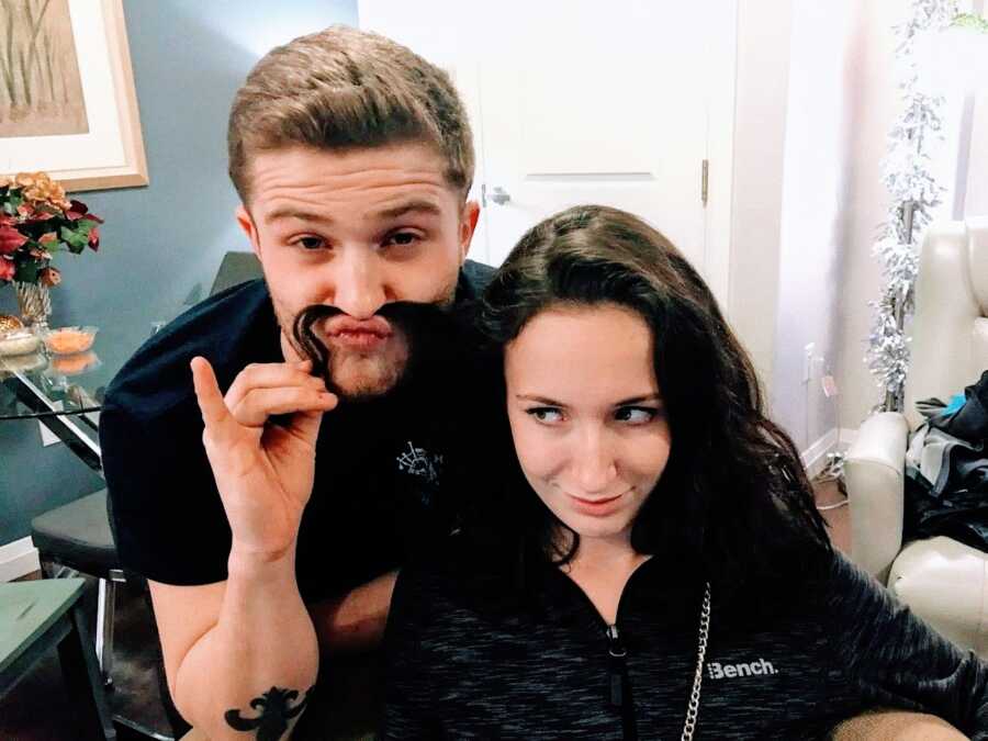 Older brother takes a silly selfie with his only sister, making himself a fake mustache with her long hair