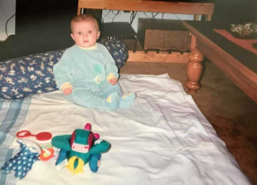 first-time mom snaps photo of her young son sitting up on a blanket on the floor in a blue onesie