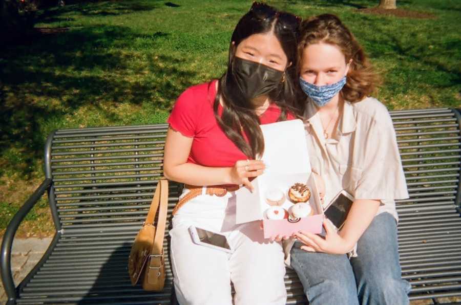 Two masked girls holding a box of cupcakes