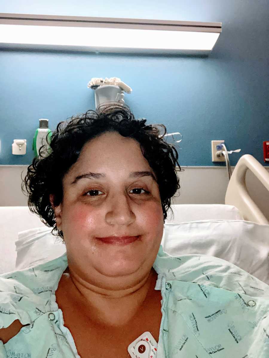 Woman sitting in a hospital bed smiles for a selfie after contracting COVID-19