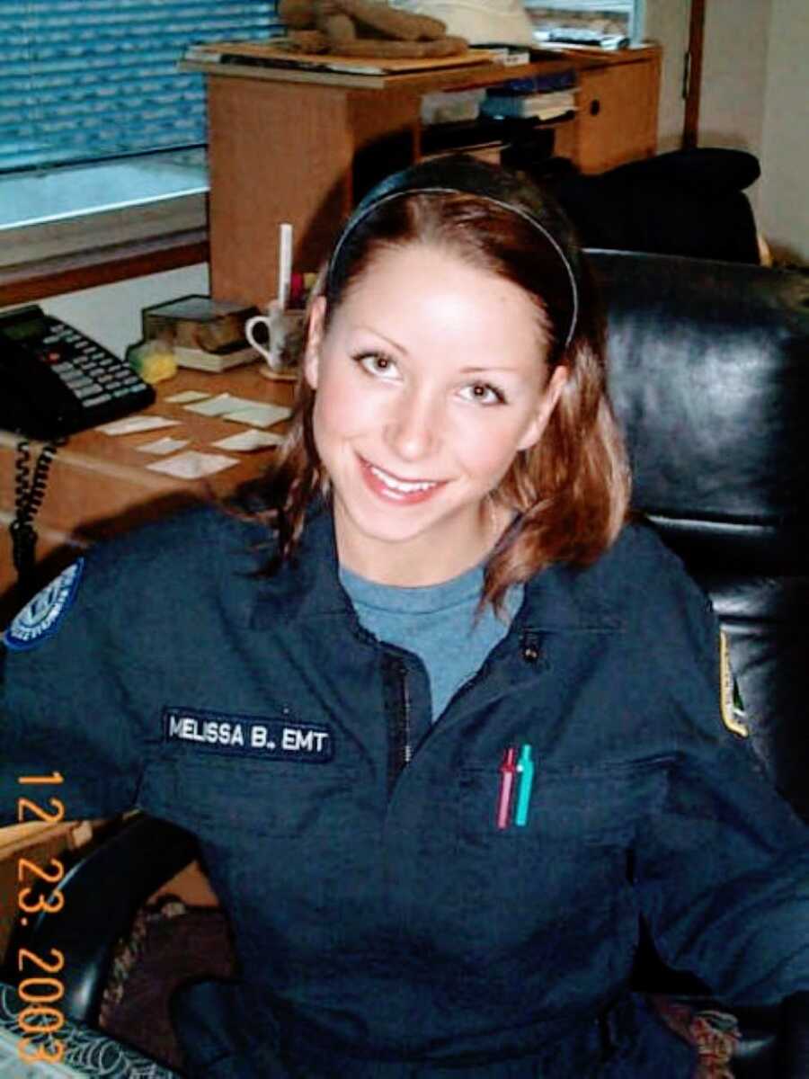 Young woman unknowingly battling autism smiles for a photo at her desk with her EMT uniform on