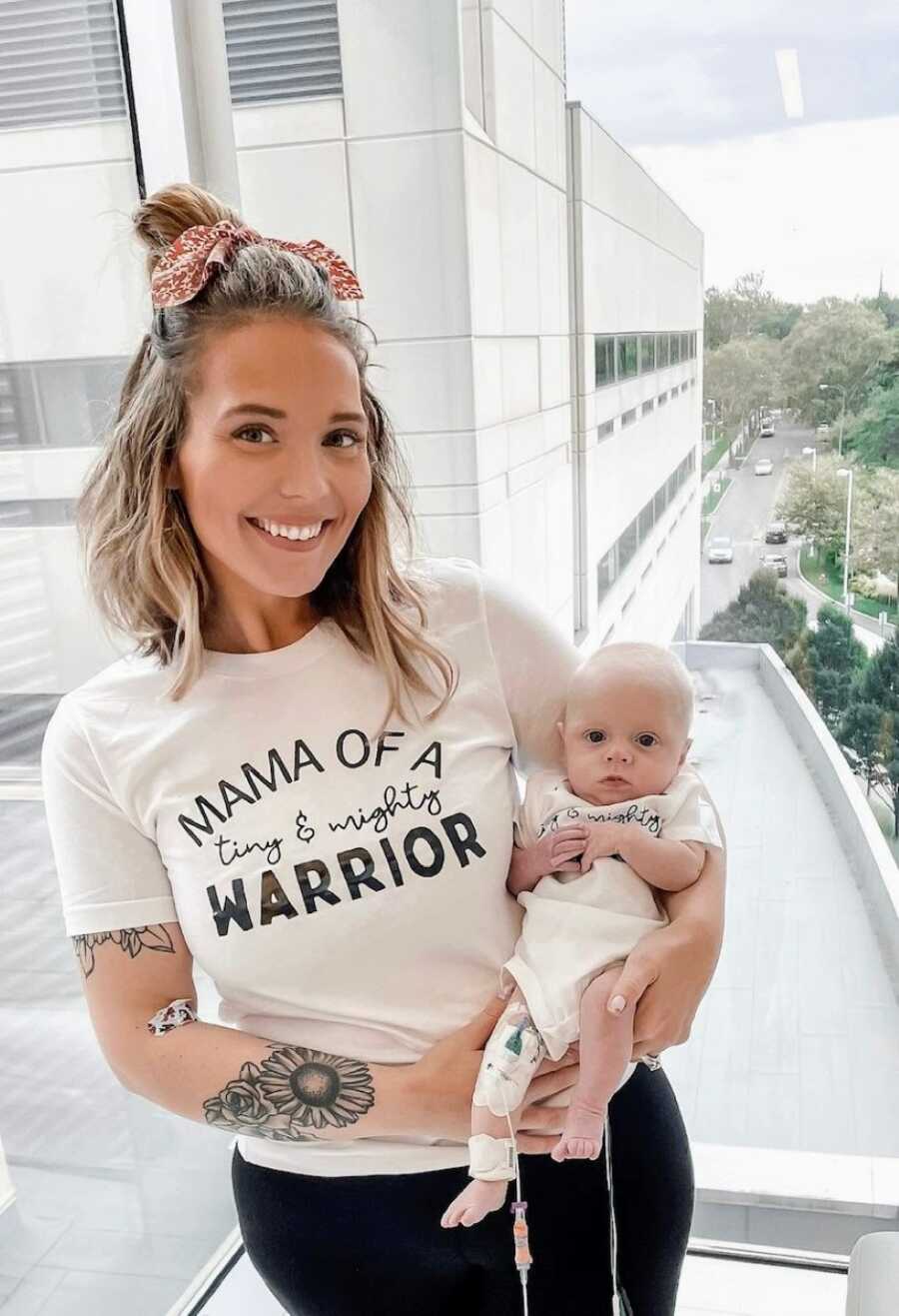 Mom holds her newborn son, a preemie and NICU warrior, in the hospital wearing matching "tiny & mighty warrior" shirts
