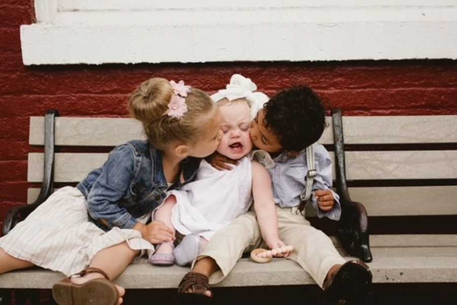 Little kiss each kiss their newest baby sister on the cheek during a family photoshoot