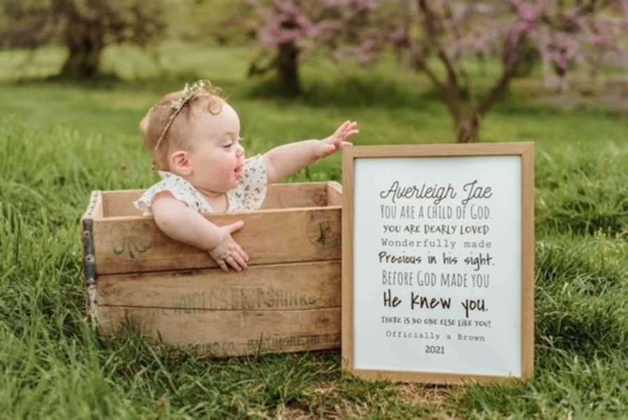 Little girl adopted out of foster care sits in a box with a sign next to her