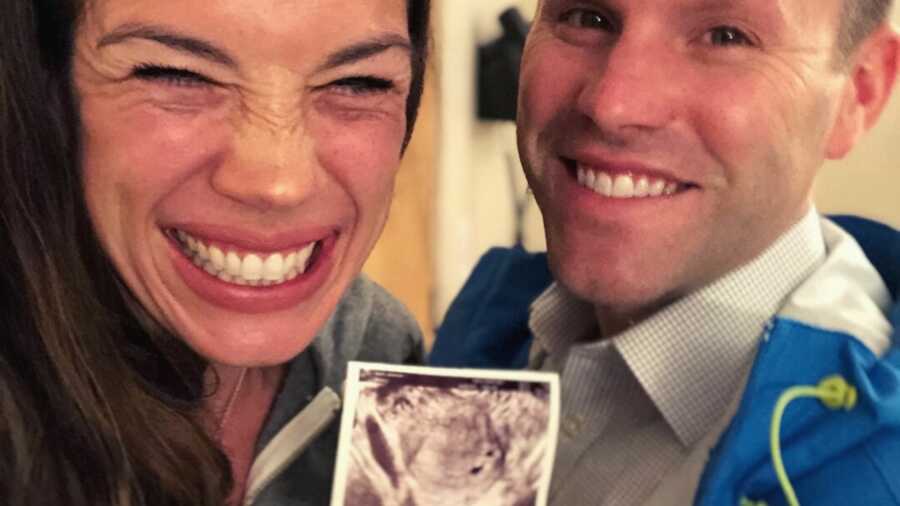 Wife grinning widely while holding up first ultrasound picture next to husband