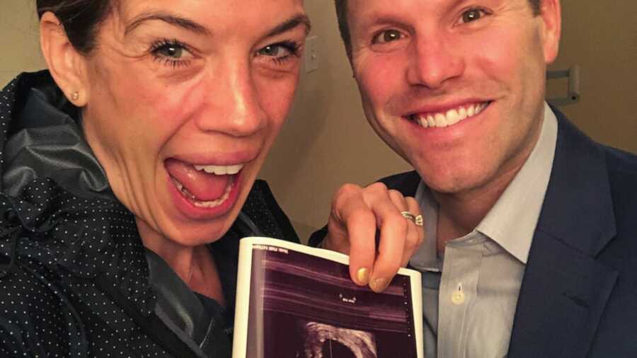 Wife holding up second ultrasound picture next to husband in suit