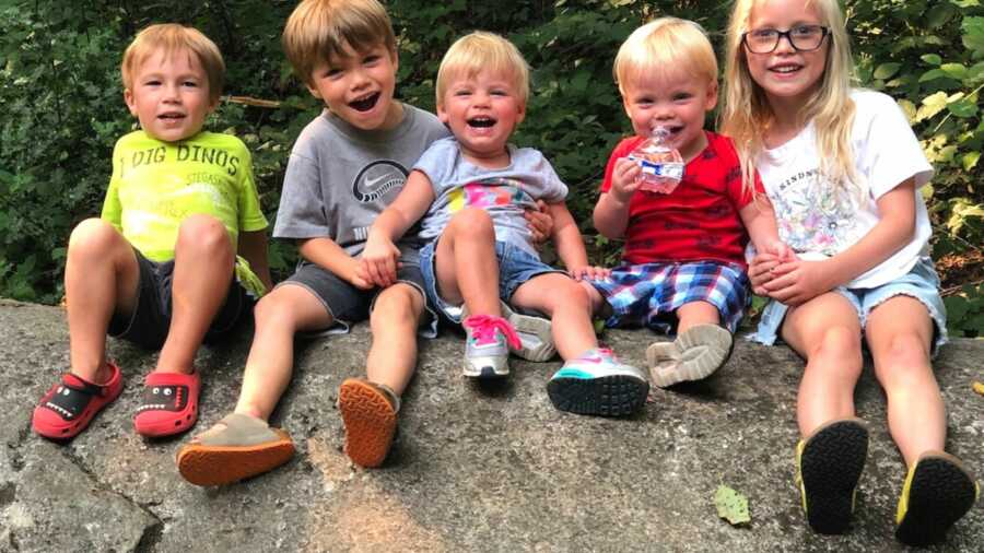 Family of four boys and one girl sitting on rock outside