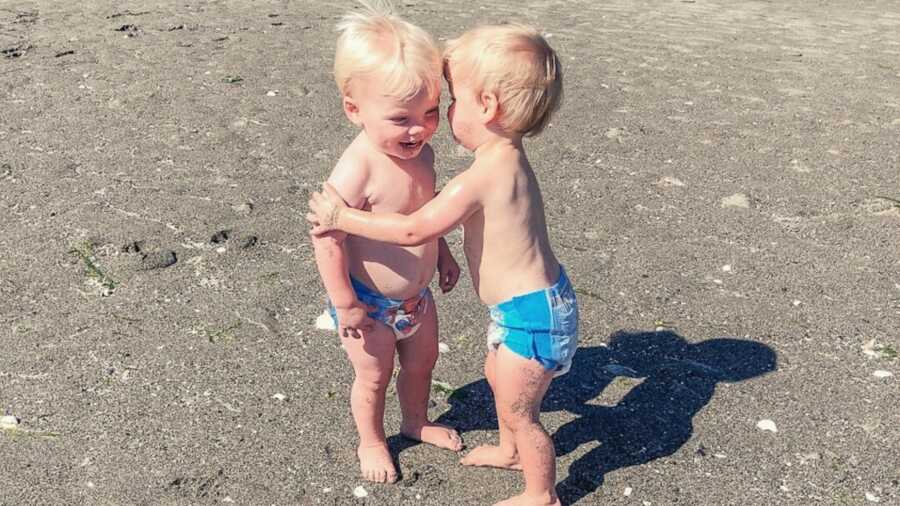 Twin boys hugging on sand at beach