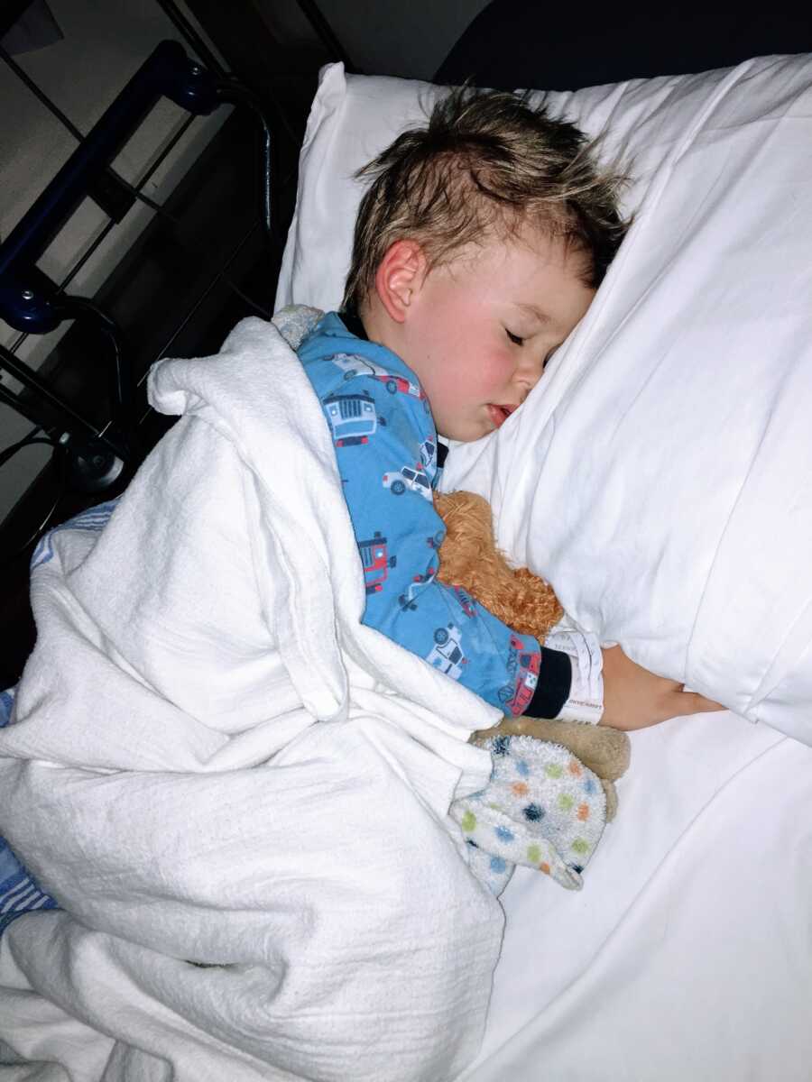 Little boy suffering from unknown seizures sleeps in a hospital bed while snuggling a stuffed animal