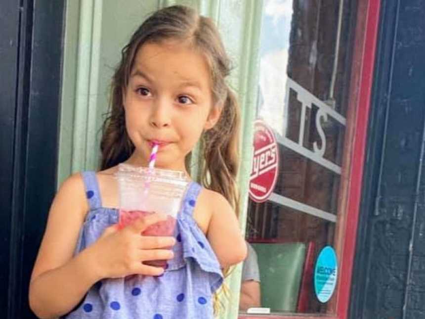 Sassy little girl with a limb difference poses with her smoothie while her mom takes a photo