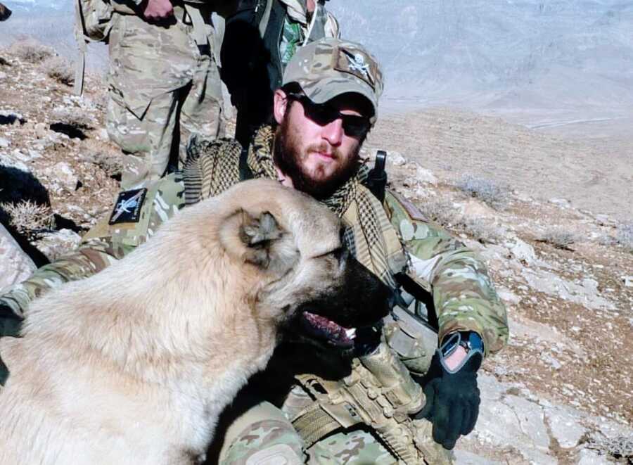 Man serving in Afghanistan takes a photo in full uniform out on a mission with a German Shepherd