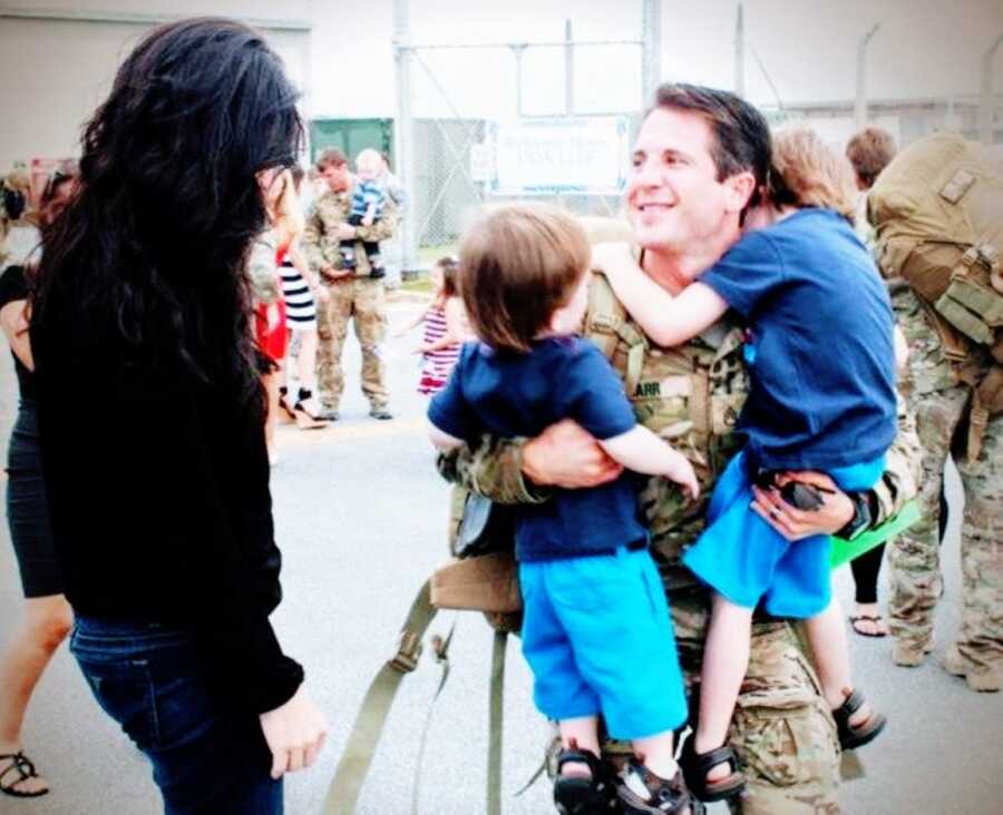 Young dad serving in the military hugs his sons and his wife after returning from Afghanistan