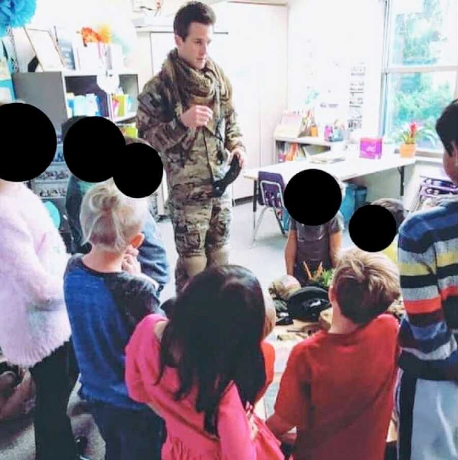 Man serving in Afghanistan stands in uniform while talking to children in a classroom