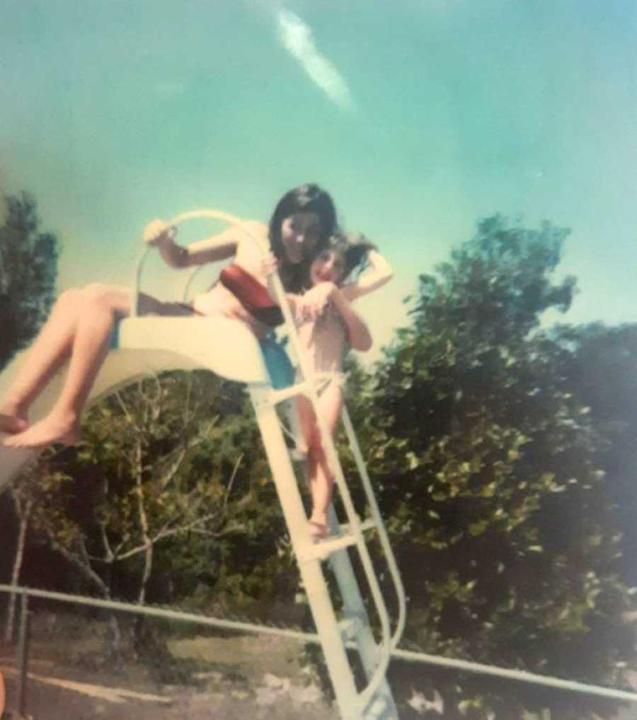 Little girl takes a photo with her mom while climbing up a pool ladder, enjoying a hot summer day together