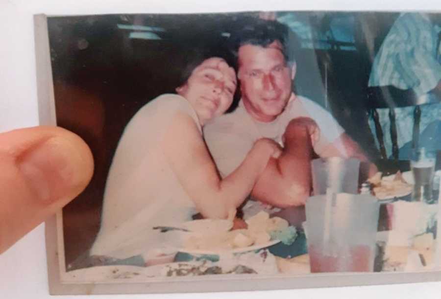 Woman takes a photo of a polaroid of her mom and her soulmate snuggled together at dinner