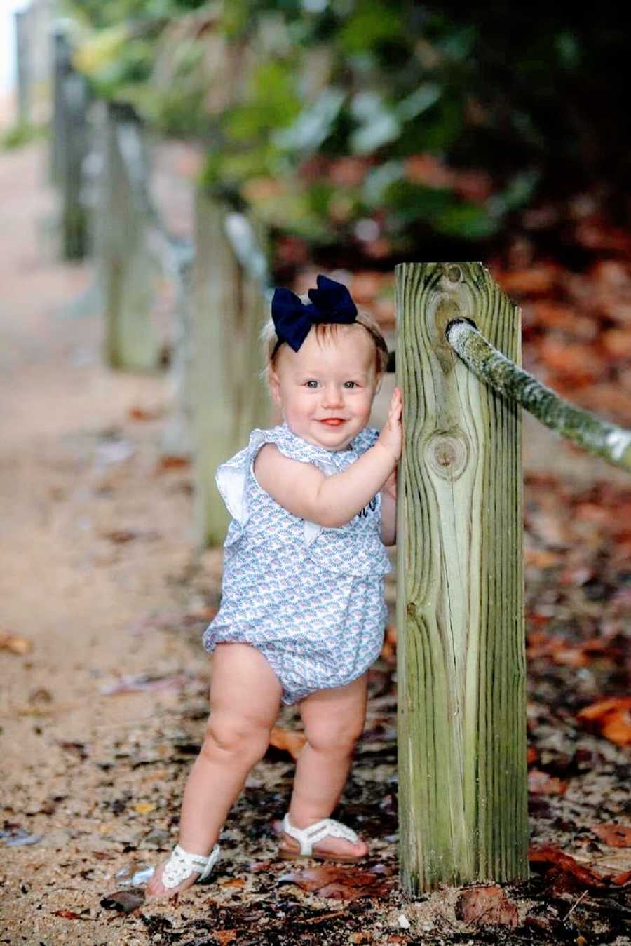 A little girl stands by a fence post