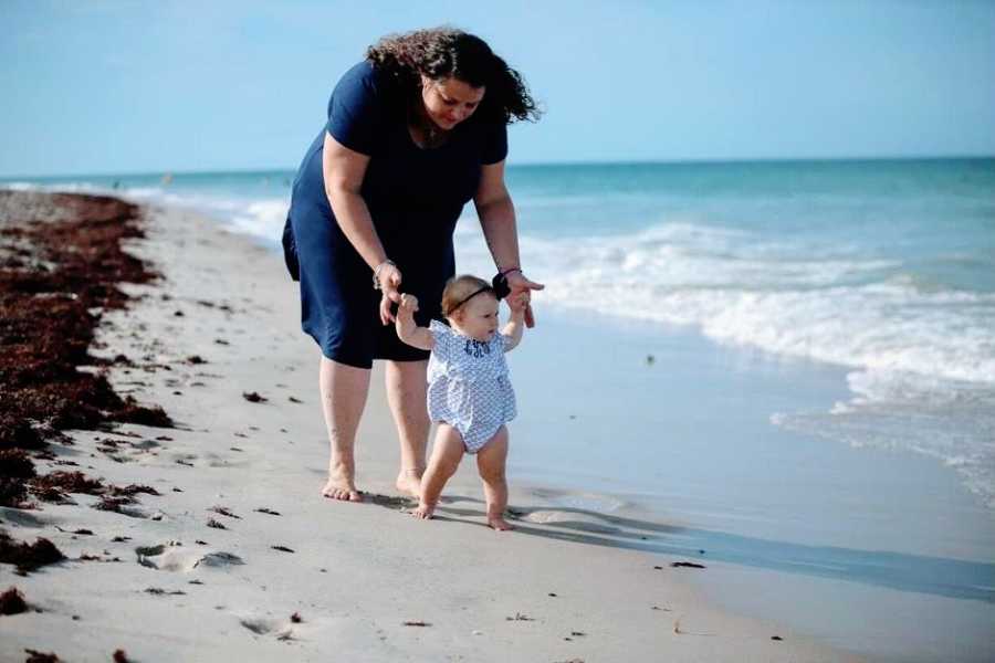 A mother helps her daughter walk along the beach