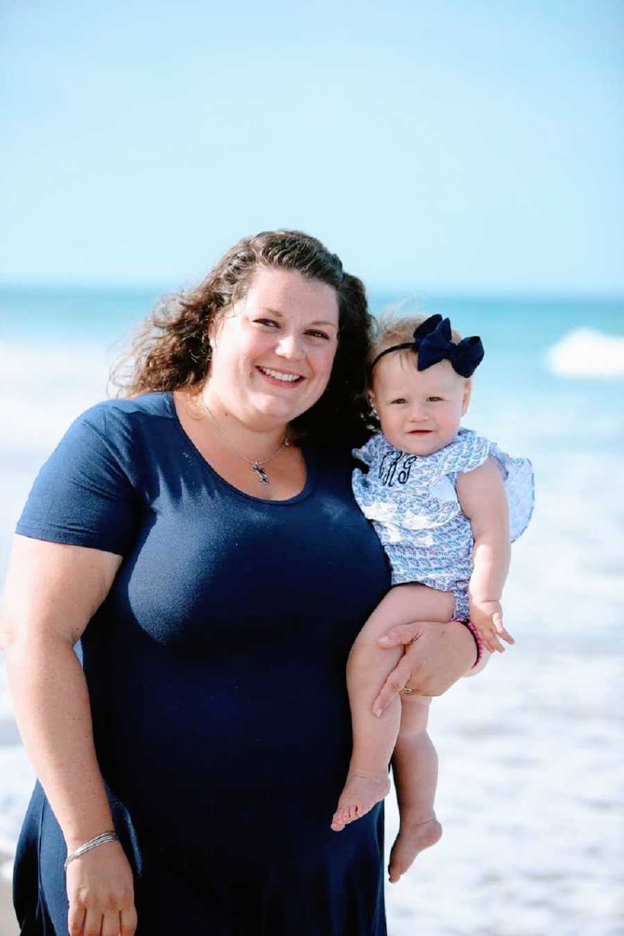 A mother holds her young daughter by the sea