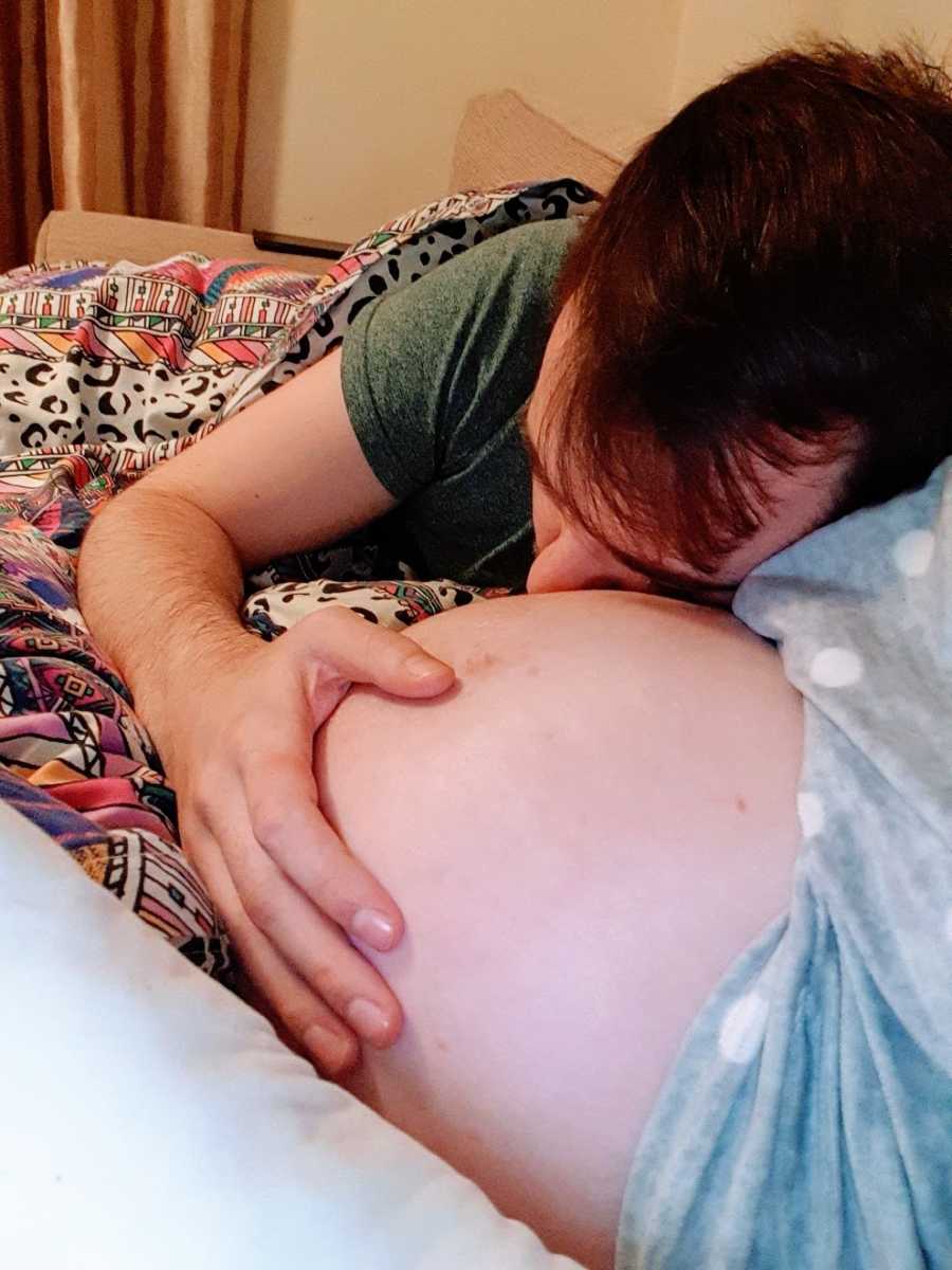 A man leans on his wife's pregnant belly