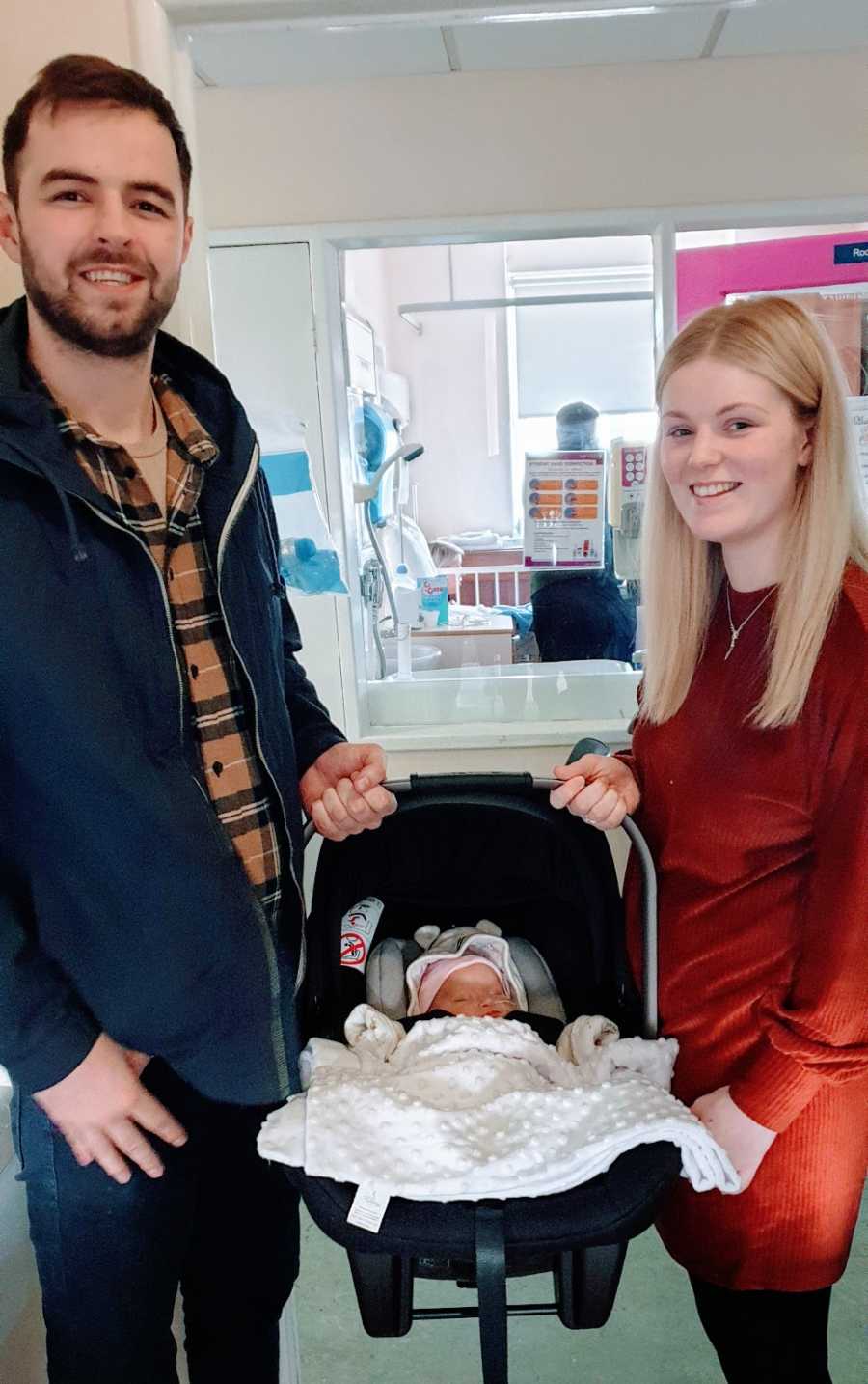 Parents hold their baby in a carrier at the hospital