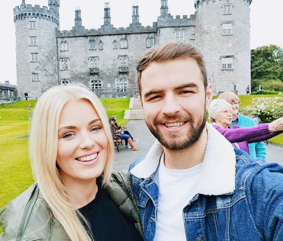 A woman and her partner stand outside an old castle