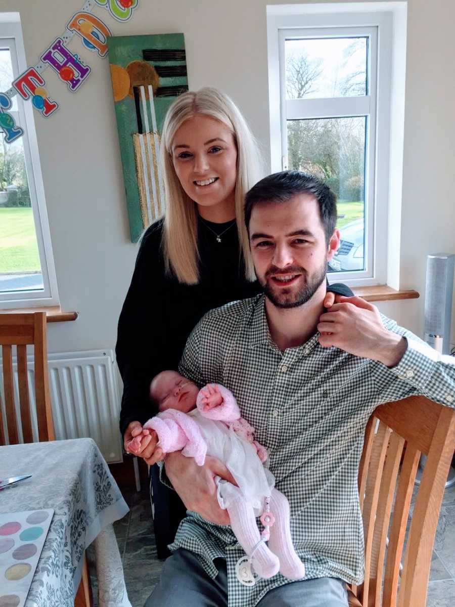 A father holds his newborn while his partner puts her hand on his shoulder