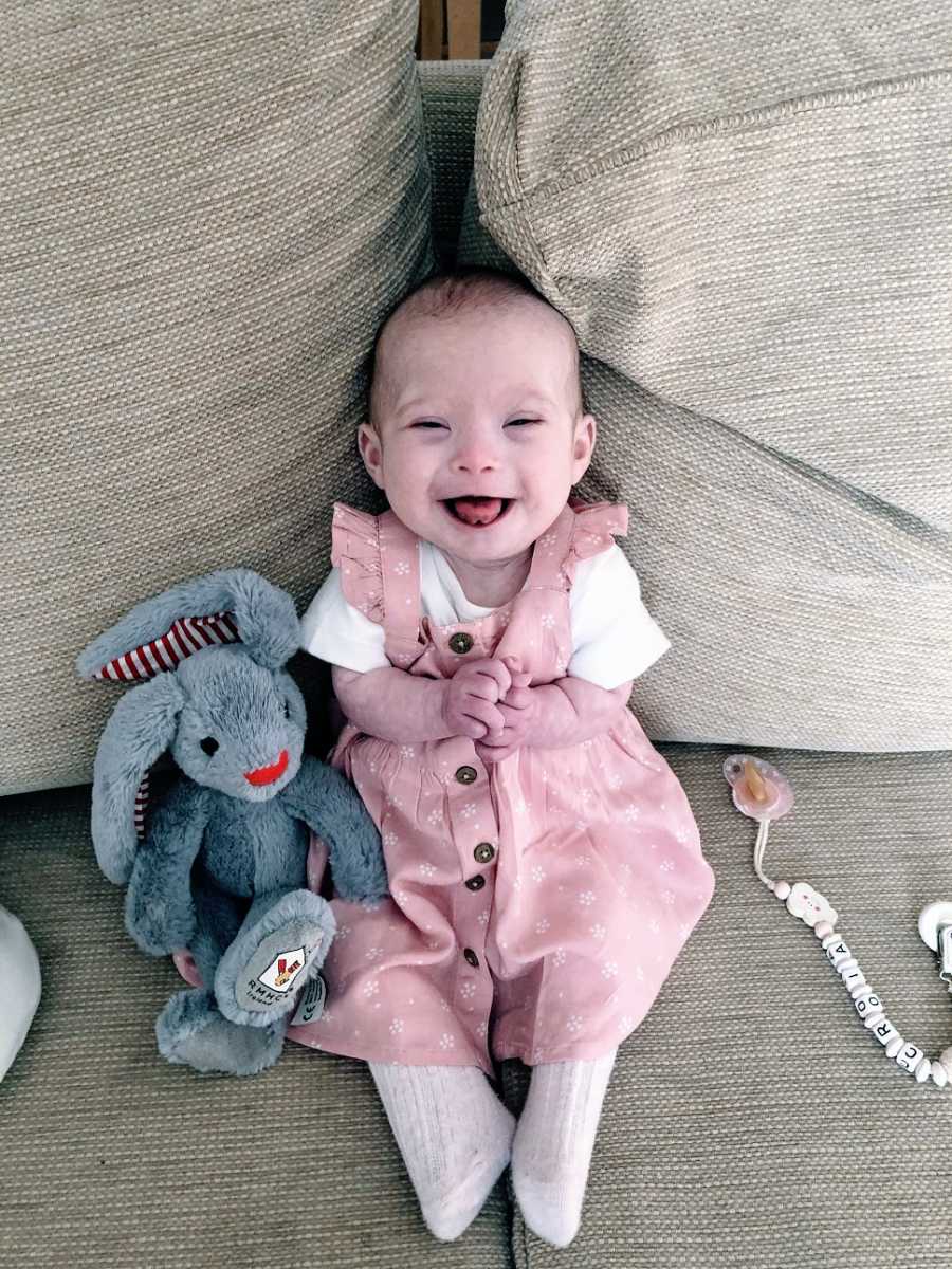 A little girl with Down Syndrome sits on a couch with a toy rabbit