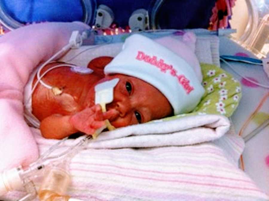 A baby girl wearing a pink hat lies in the NICU