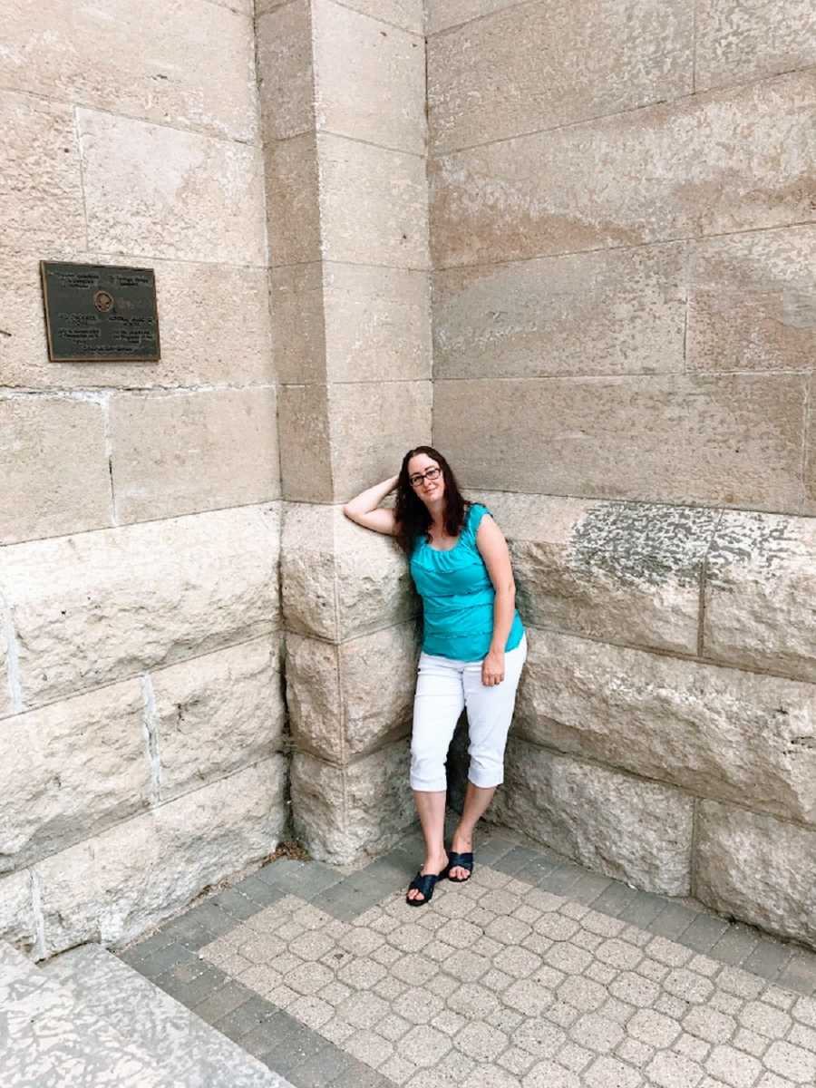 Woman wearing blue tank top stands by wall
