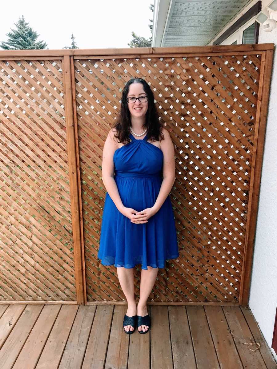 Woman wearing blue dress stands by fence