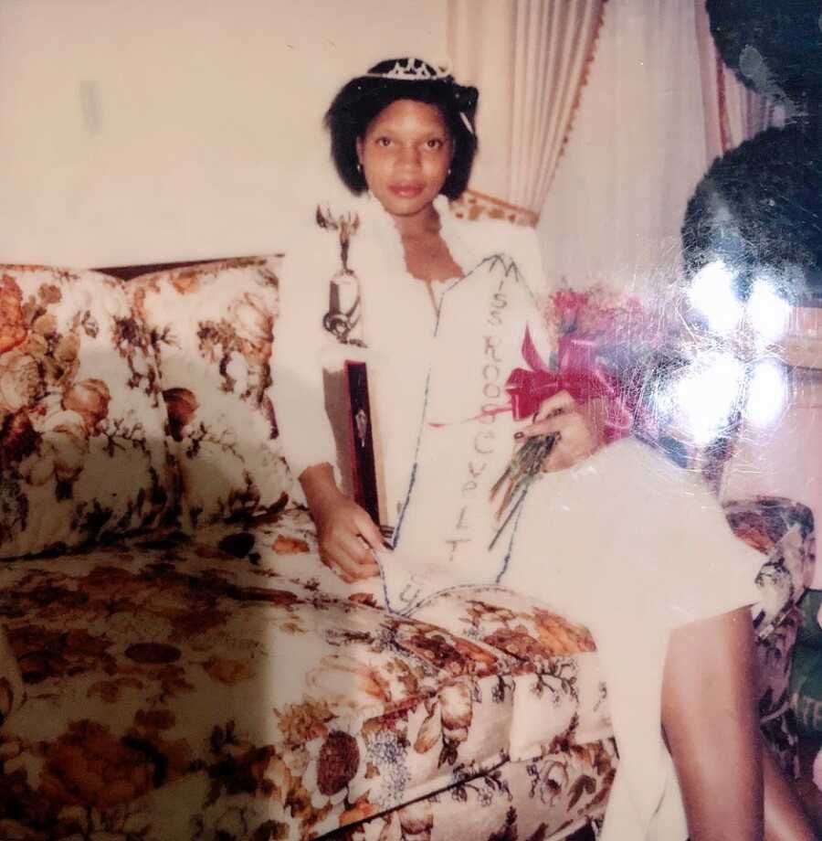 Young woman holding trophy and bouquet sits on couch