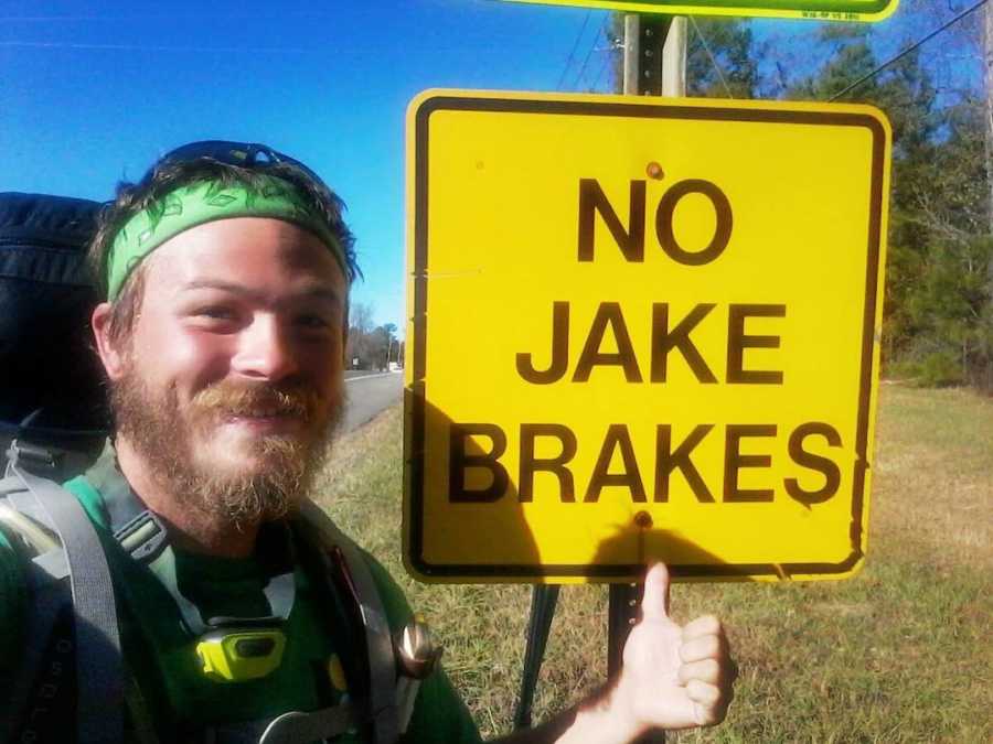 homeless man smiling next to a sign 