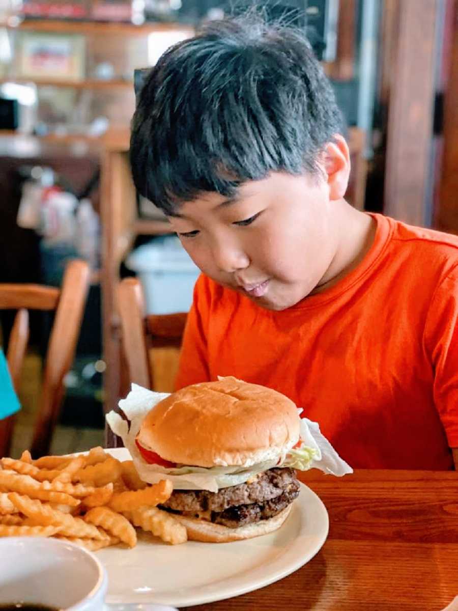 Boy in red shirt looks at hamburger on plate