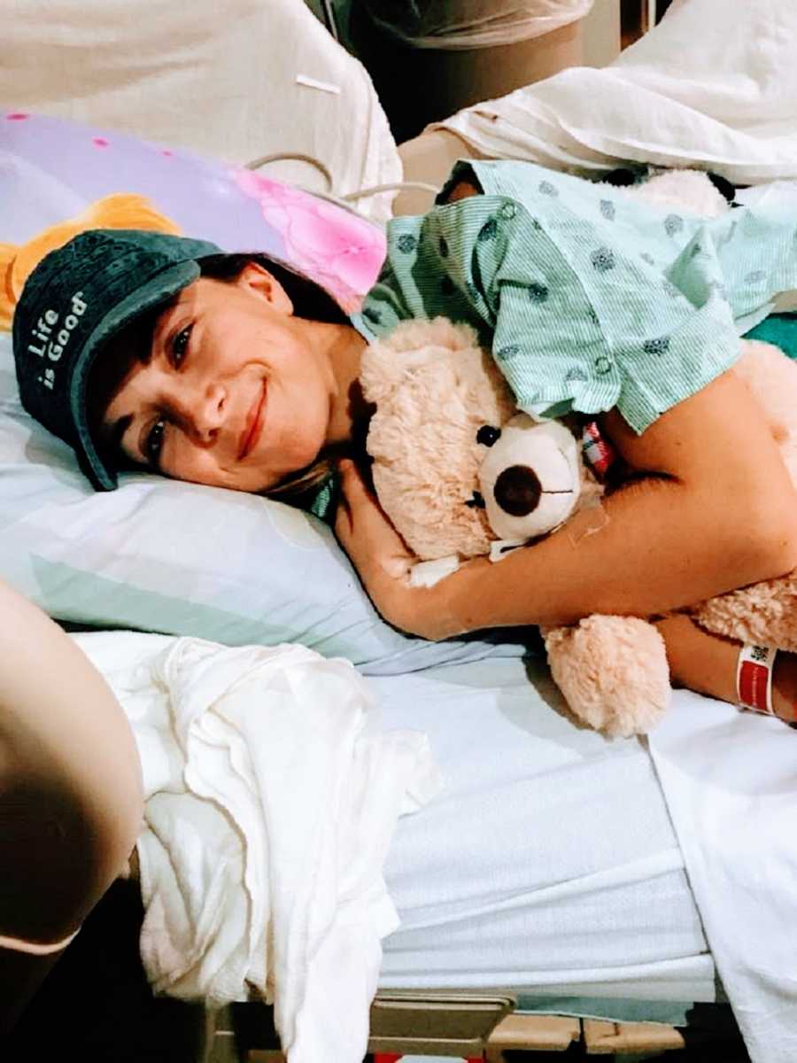 Chronically ill woman lying in hospital bed with teddy bear