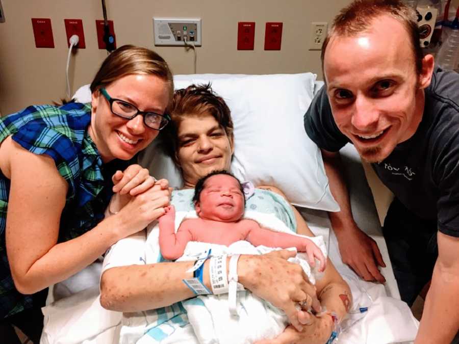 在医院里，一对父母站在一位生母和她的新生儿旁边