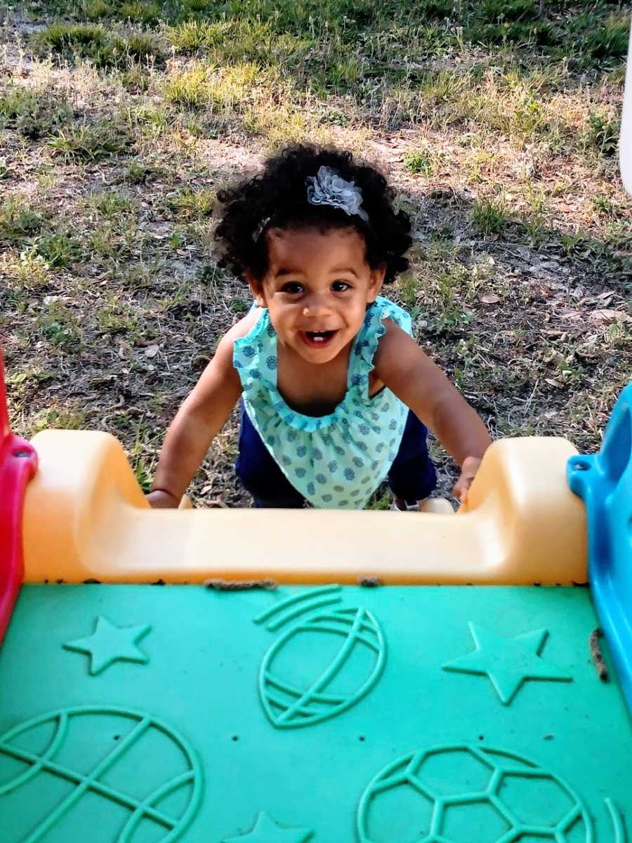 A little girl climbs up a plastic play slide