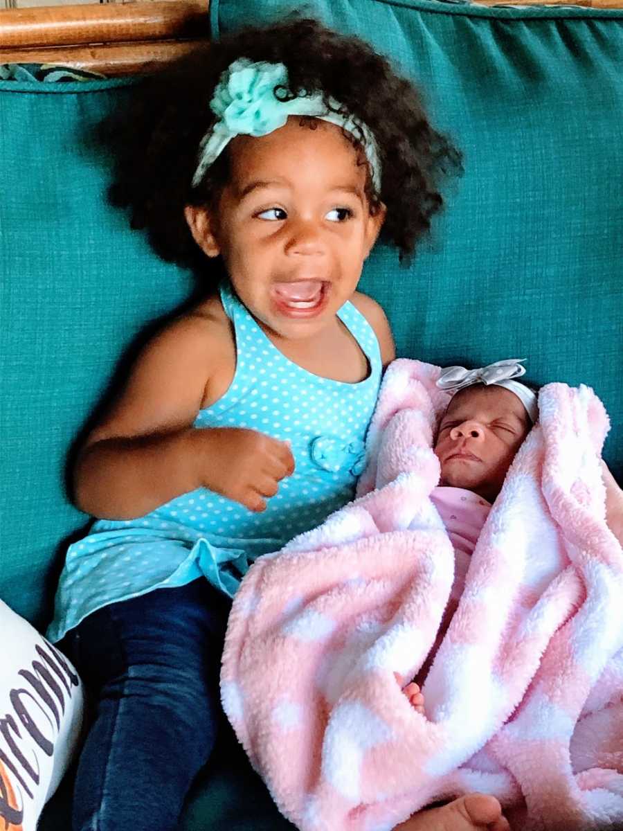 A little girl sits next to her baby sister on a blue couch