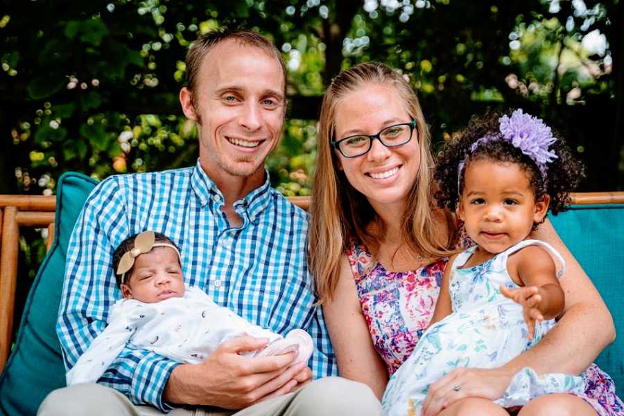 Parents hold their two adopted daughters outside