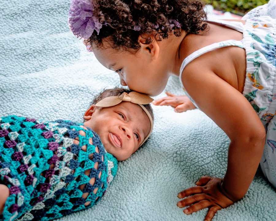 A little girl kisses her baby sister on the forehead