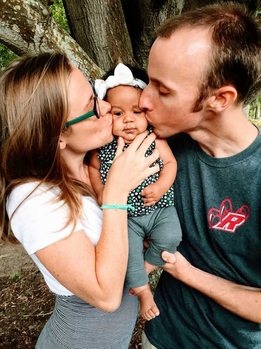 Parents kiss their baby girl on either cheek