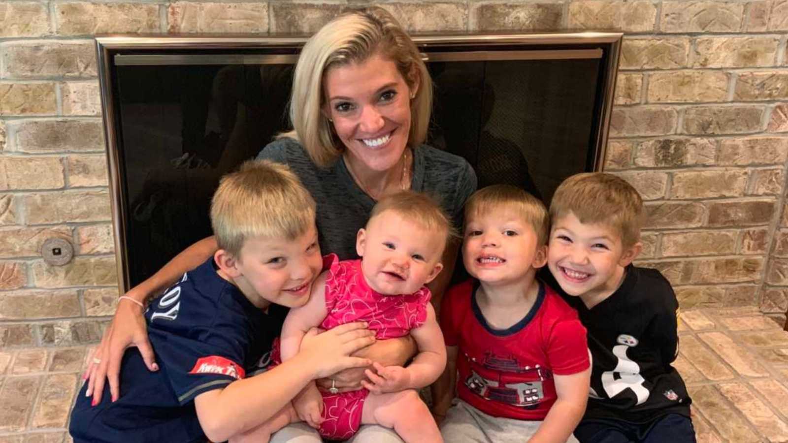 A mom sits with her four children on a fireplace