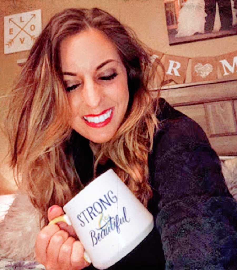 A woman wearing red lipstick smiling and holding a mug